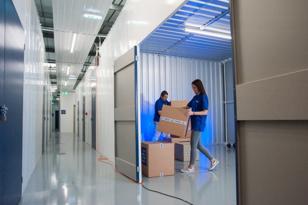 Two employees stacking cardboard boxes in a storage unit