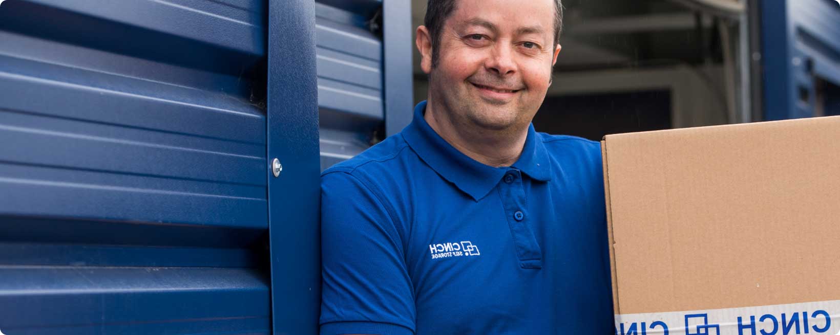 A man happily lifting a cardboard box while standing outside a storage unit