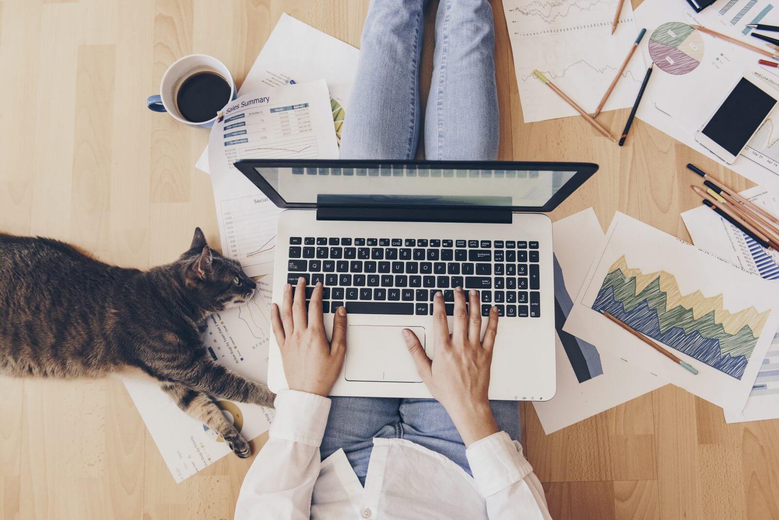 A woman working on her laptop while sitting on the floor beside her cat