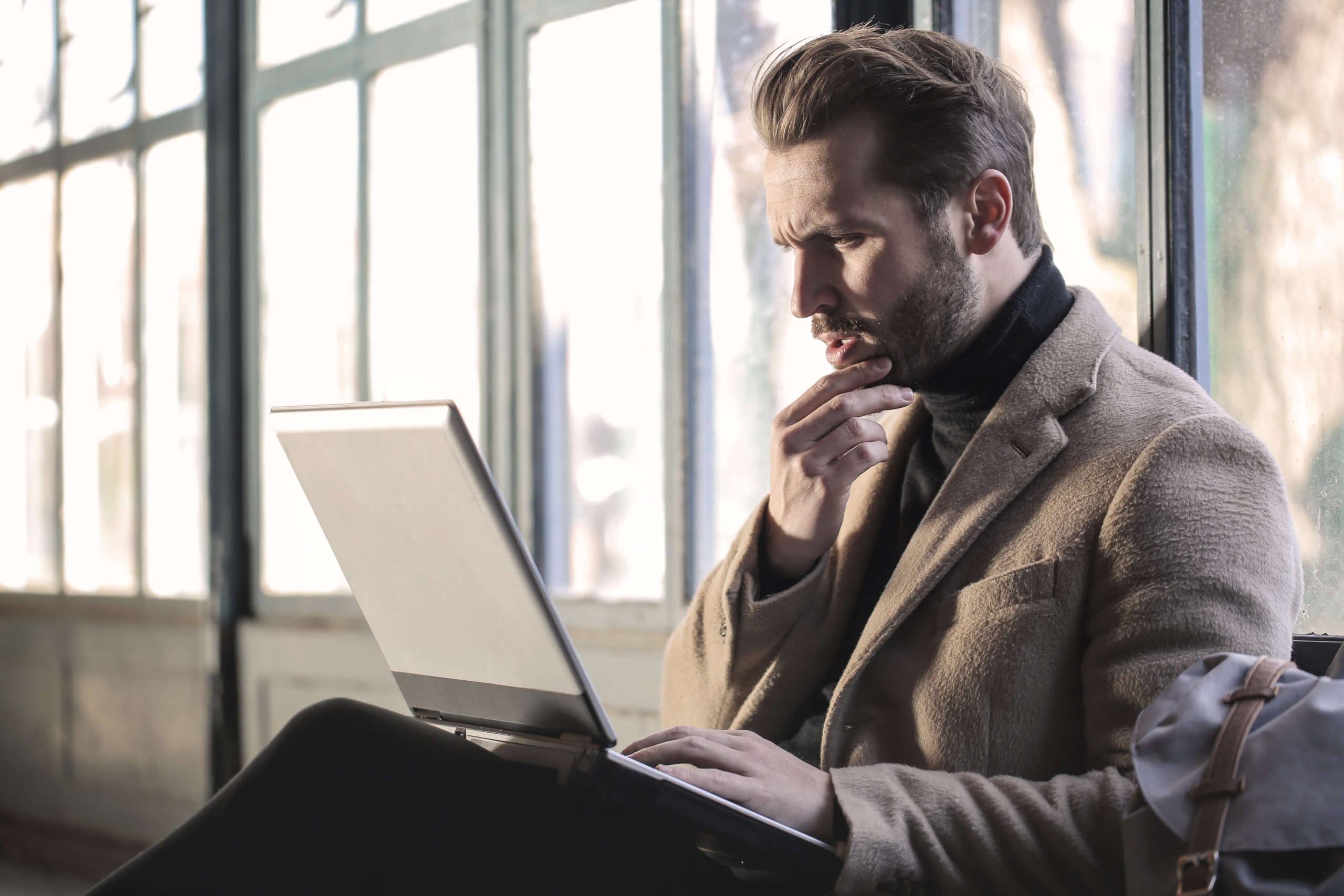 A man looking at his laptop seriously while holding his chin