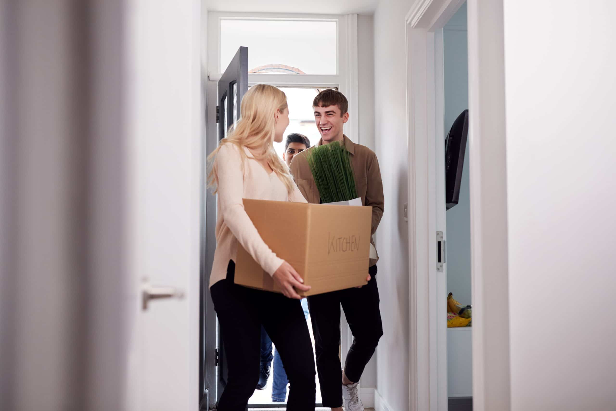 Young people walking through the front door of student housing carrying boxes