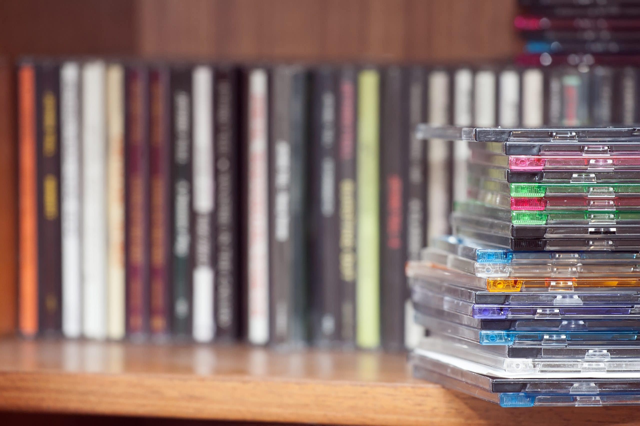 Old CDs and DVDs stacked on a wooden bookshelf