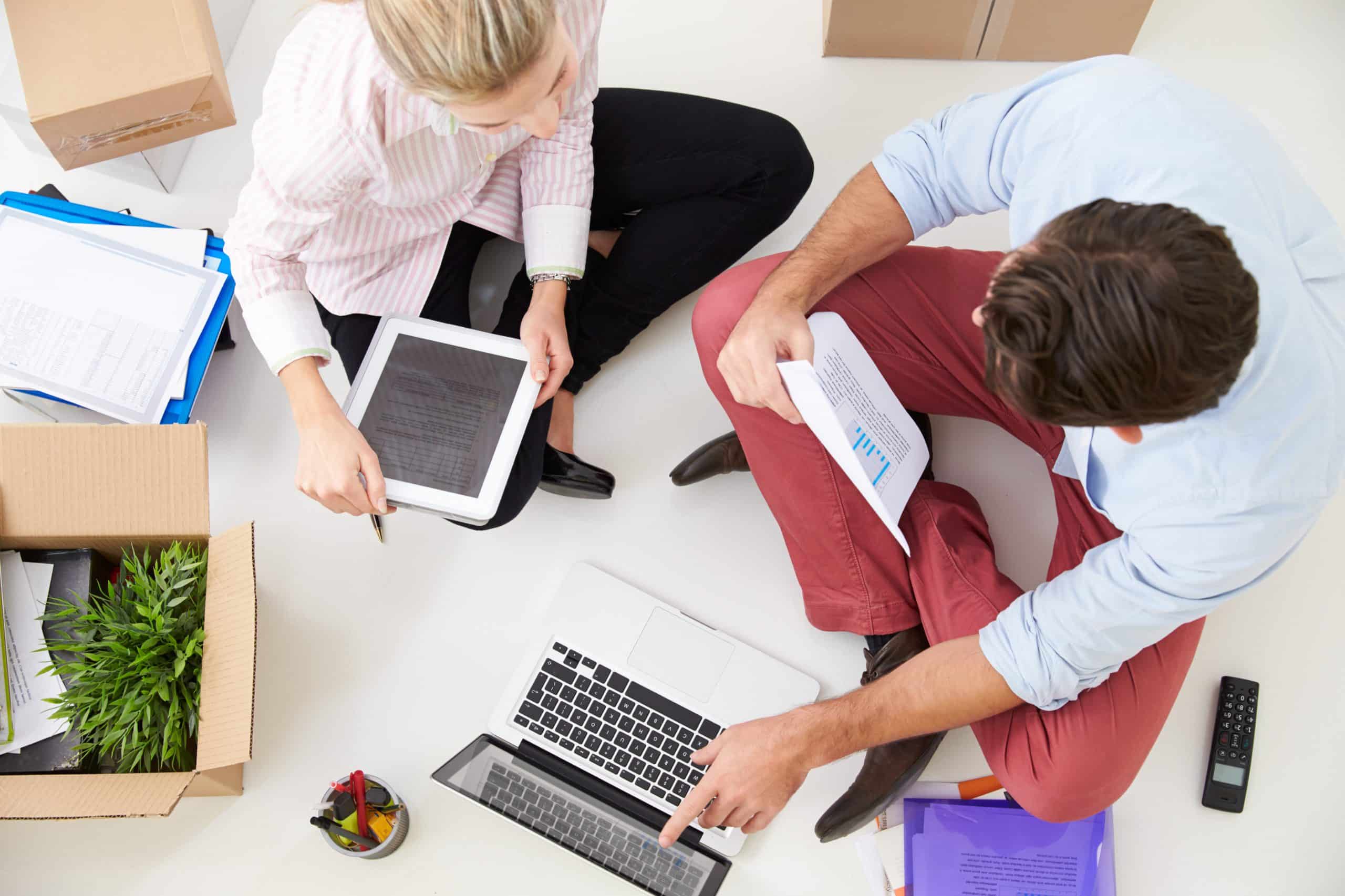 Overhead view of people without office space sat crosslegged on the floor with work stuff scattered around them