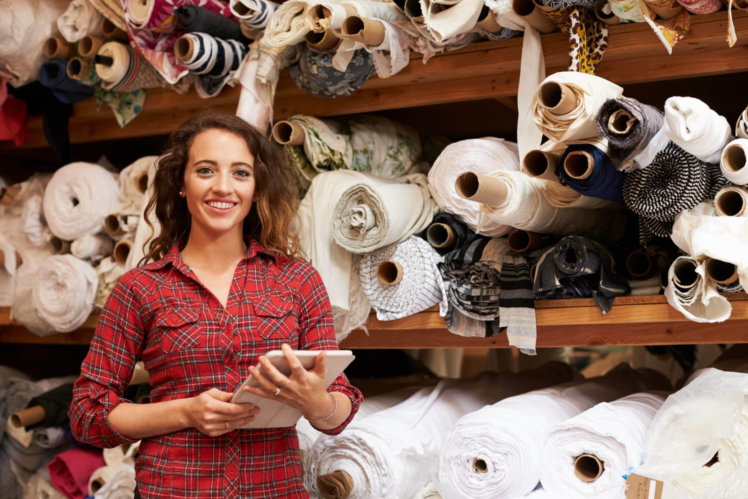 Smiling woman standing in front of shelving full of fabric using stock storage Chingford