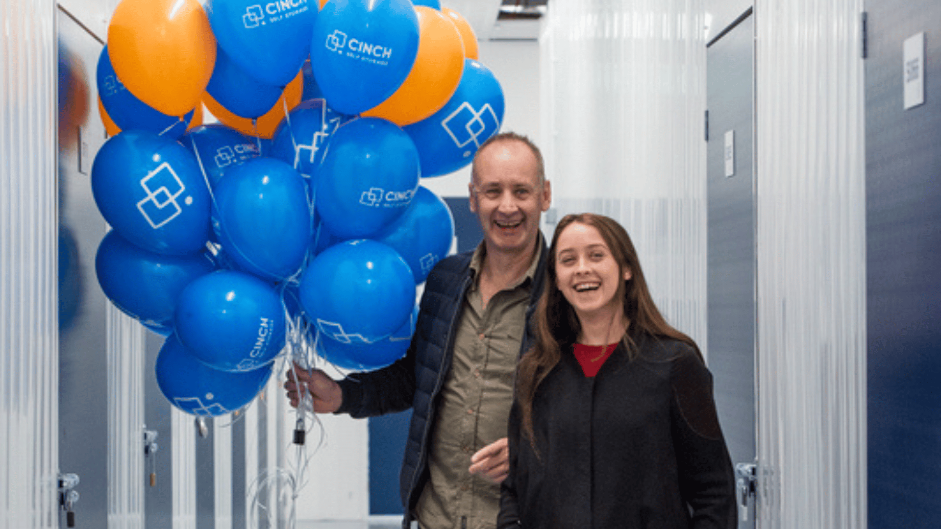 Man and girl walking down corridor in self storage Gillingham facility, smiling and holding blue and orange balloons