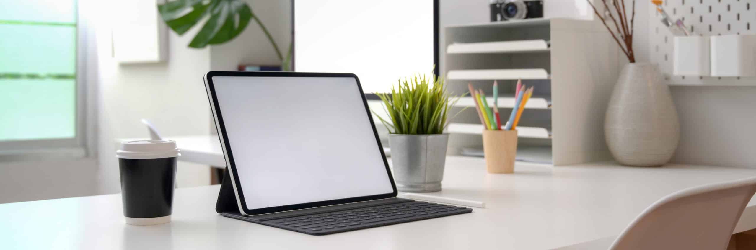 image shows office desk with open tablet, coffee cup and plants