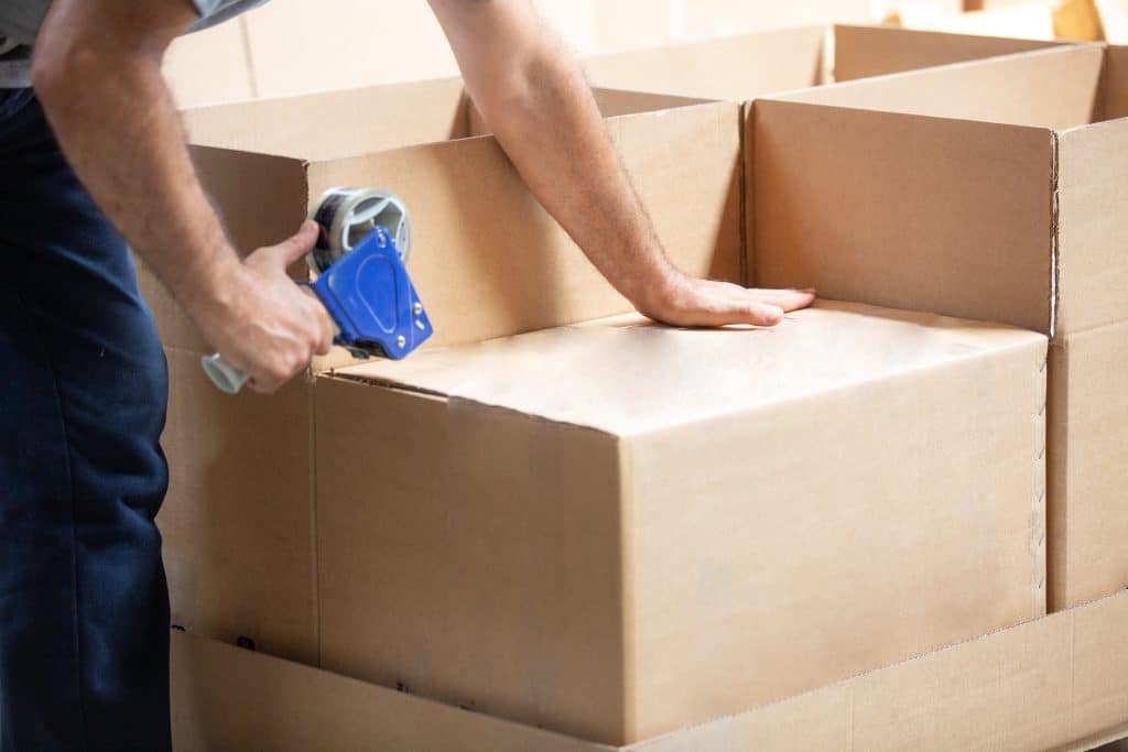 Photograph shows person taping up lots of moving boxes, going to our storage rentals near enfield 