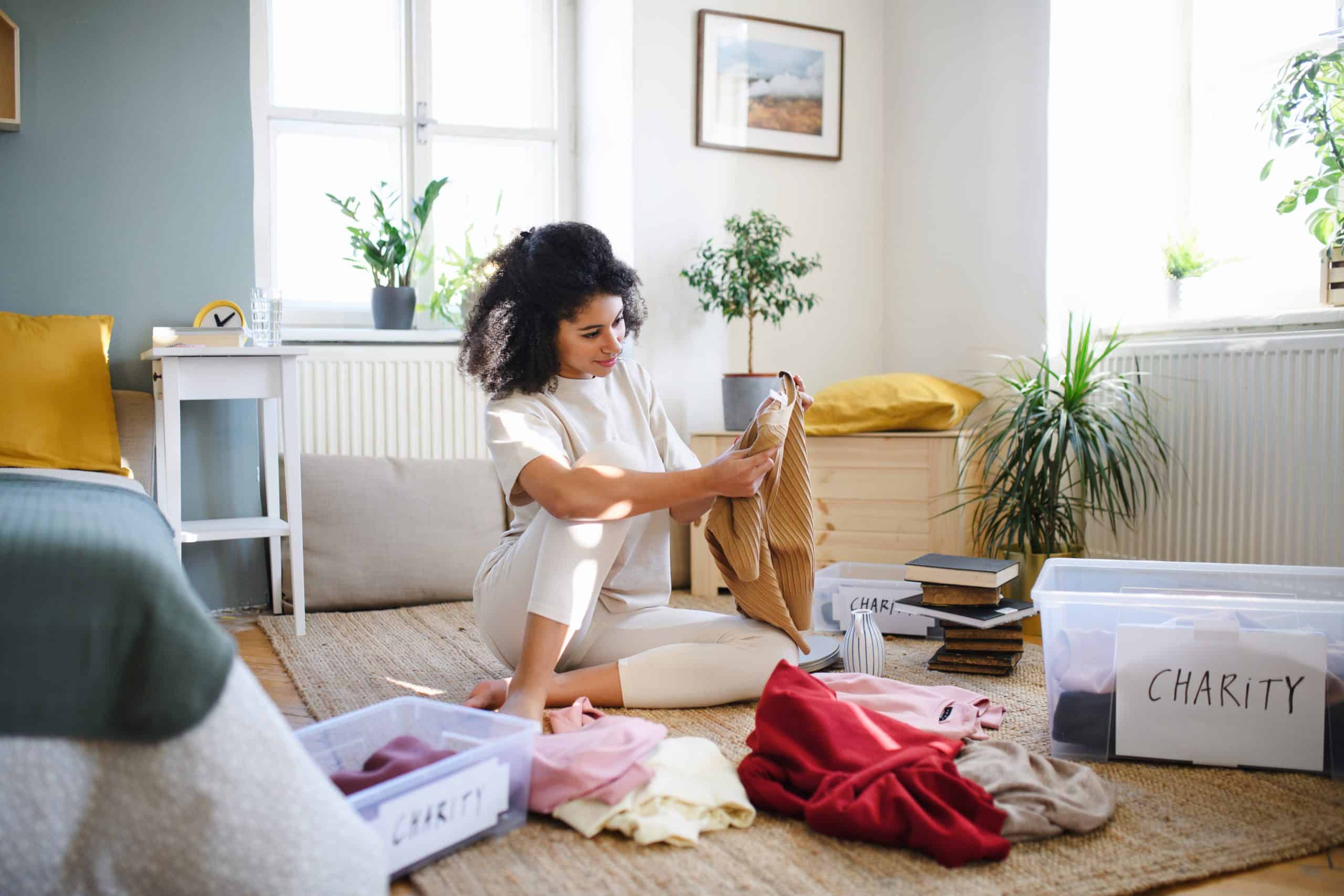 Woman sitting on the floor having a sort out of clothes surrounded by boxes ready to take to storage units to rent Mitcham