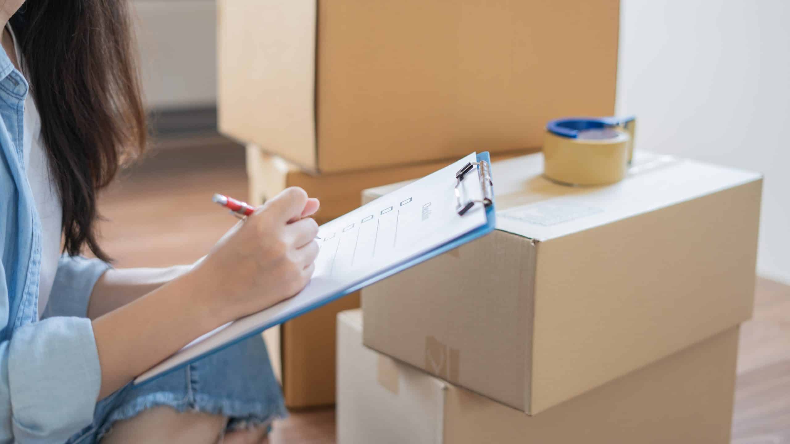 House move storage Mitcham - image shows a pile of boxes with tape on top and a woman sitting checking things off a list on her clipboard