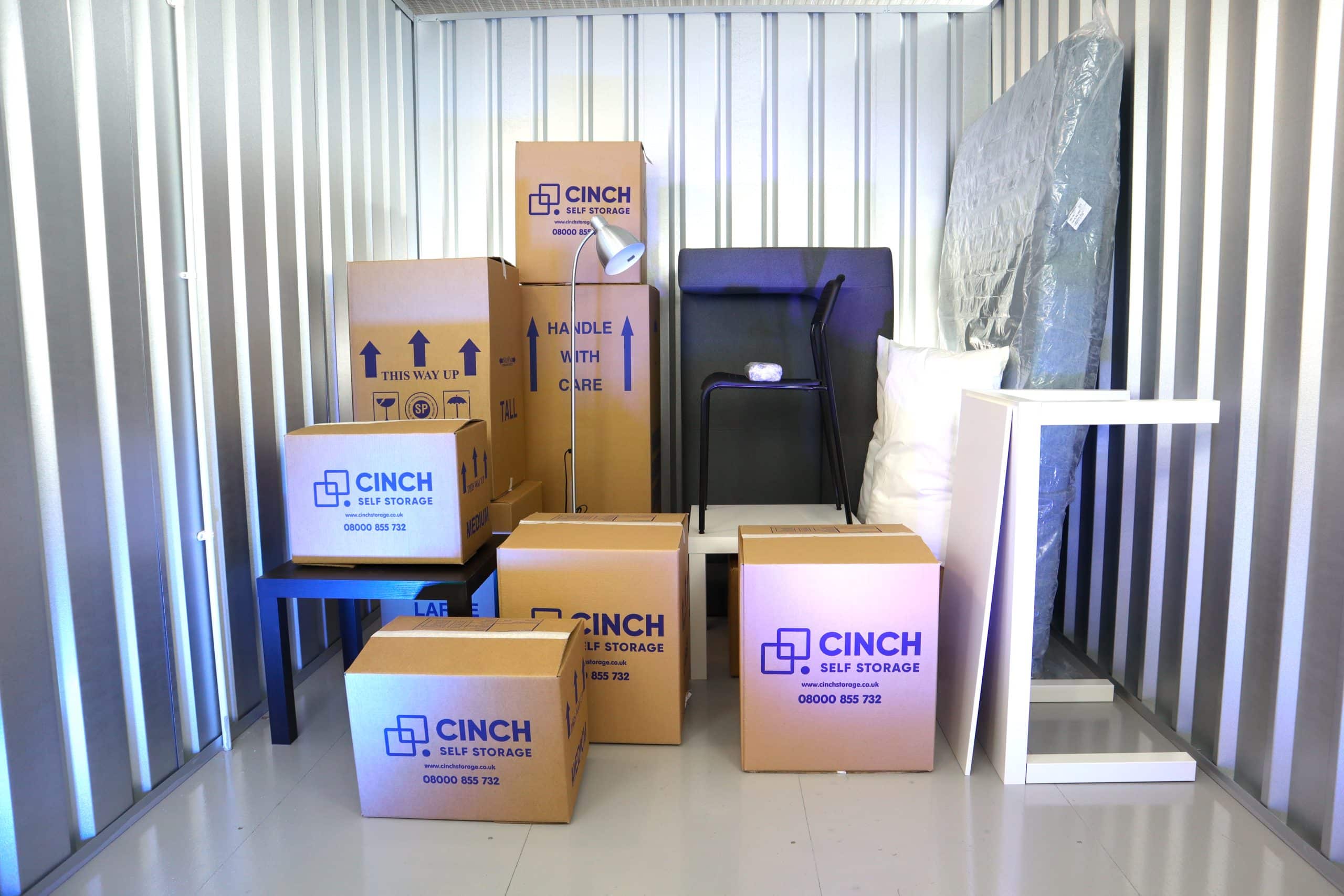 Self-storage Chingford - image shows the interior of a storage unit with Cinch Self Storage boxes stacked on top of eachother, a table on it's side and sofa on it's side