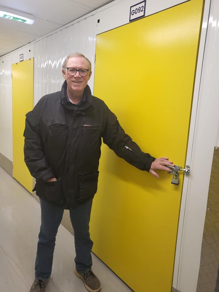 Cinch Self Storage Case Study - Photo shows a man, Cy Wells in front of his storage unit with a yellow door 