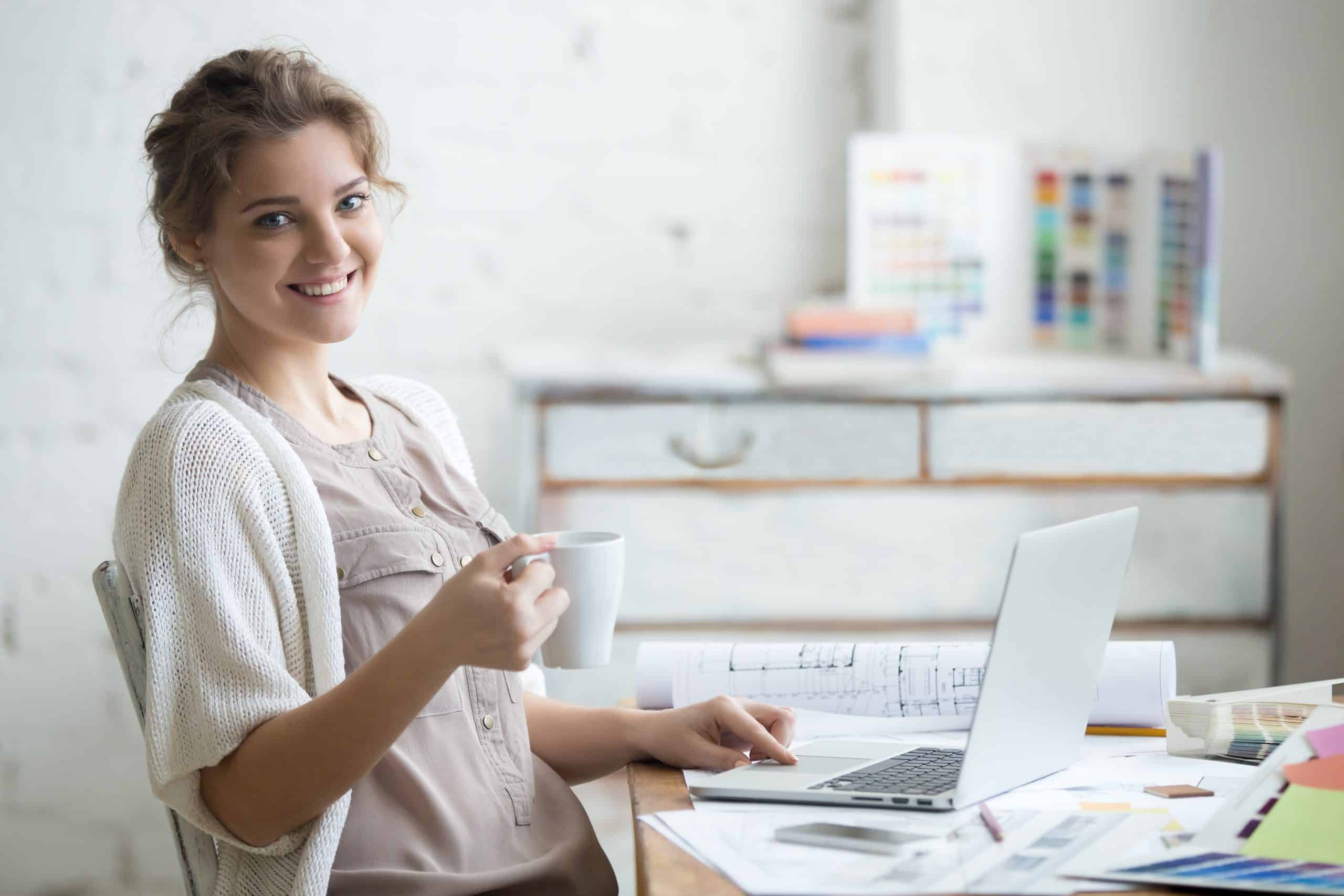 Office to rent Bicester - photo shows small business owner woman sitting at her desk, holding a cup of tea with house plans and an open laptop on the desk