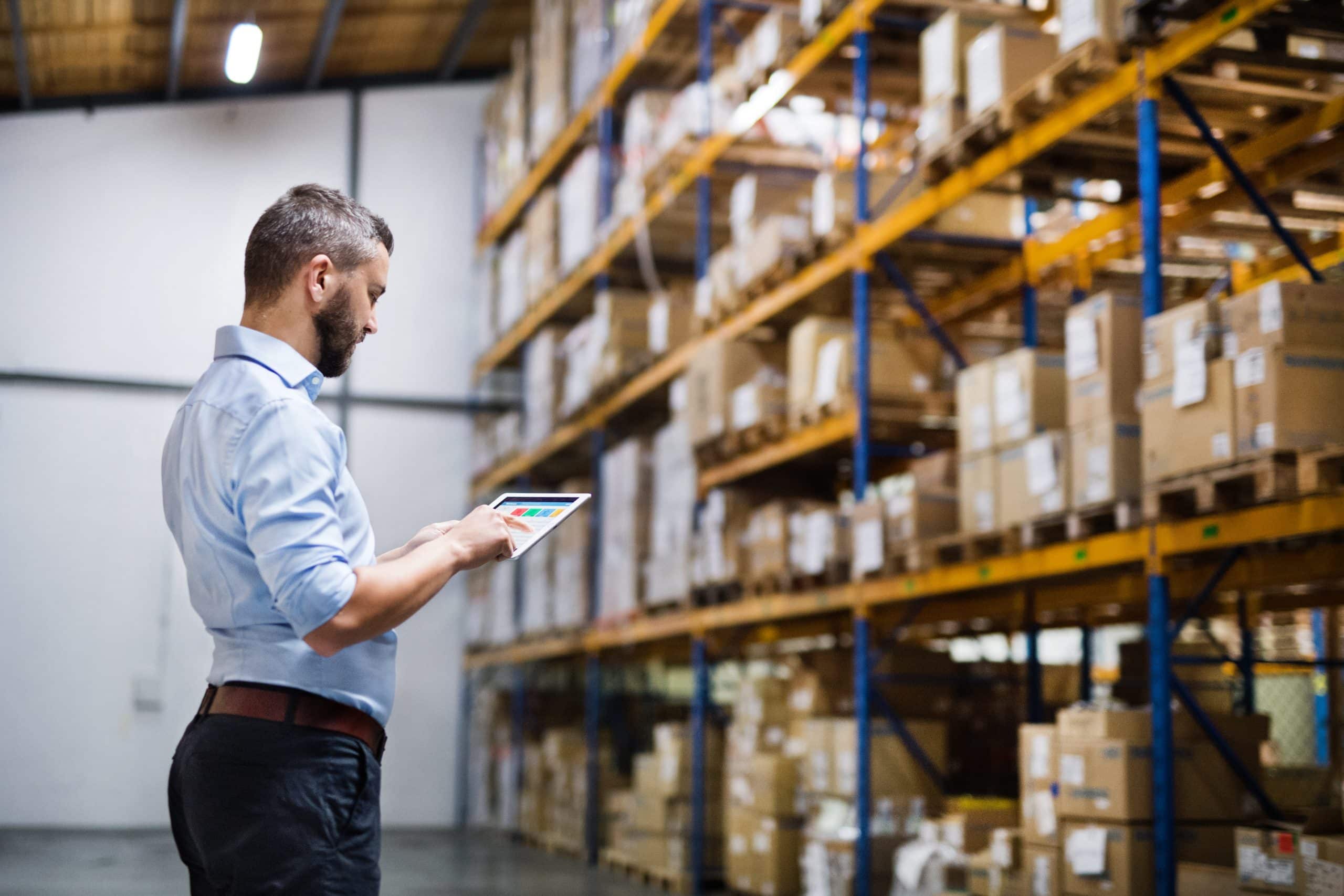 Commercial premises in Huntingdon - photo shows a man inspecting inventory within a warehouse space, pointing at an tablet with stacked boxes on racking in the background