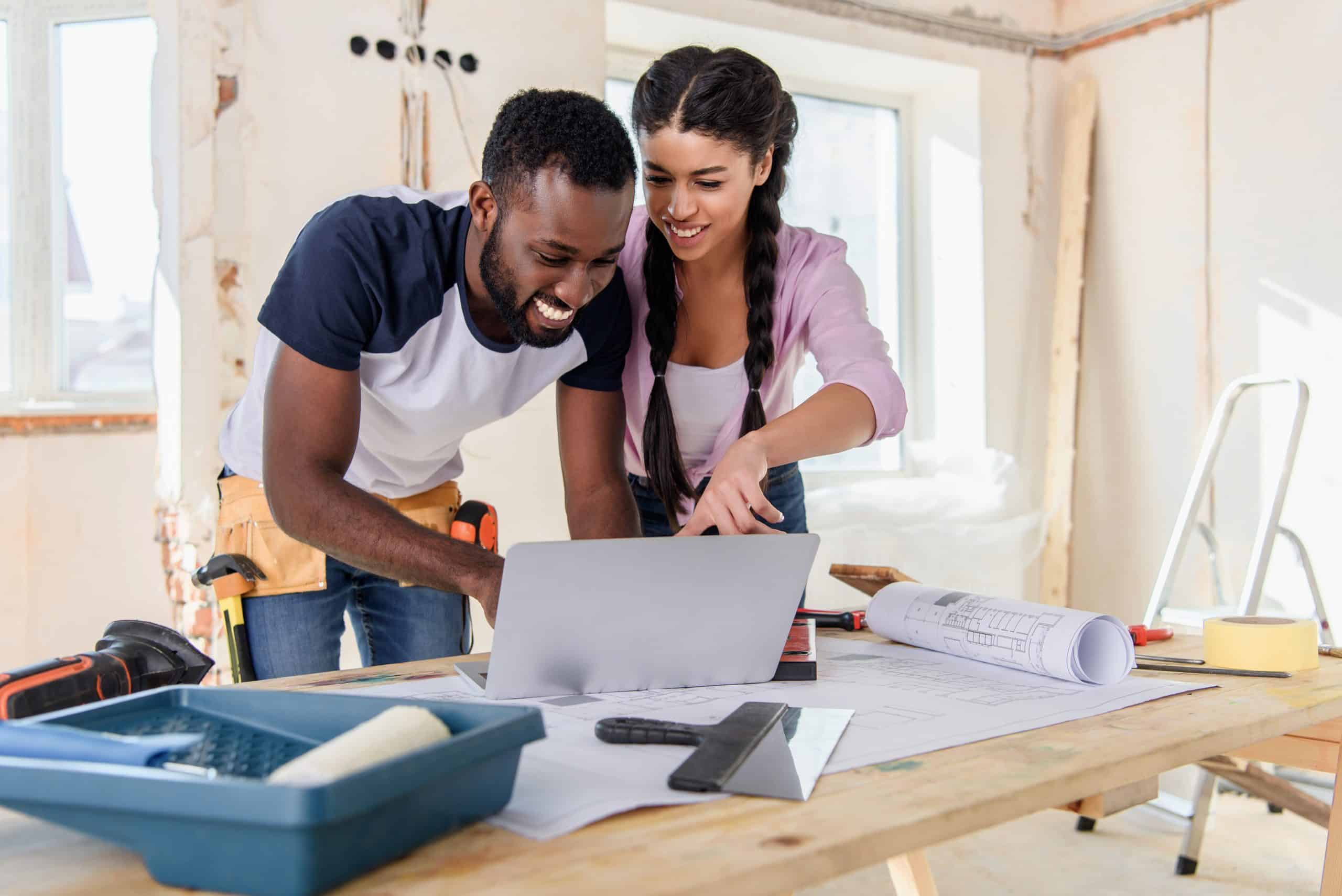 Storage Newbury UK - image shows a couple pointing at a laptop smiling with a home renovation going on in the background, with paint try and roller on the work bench