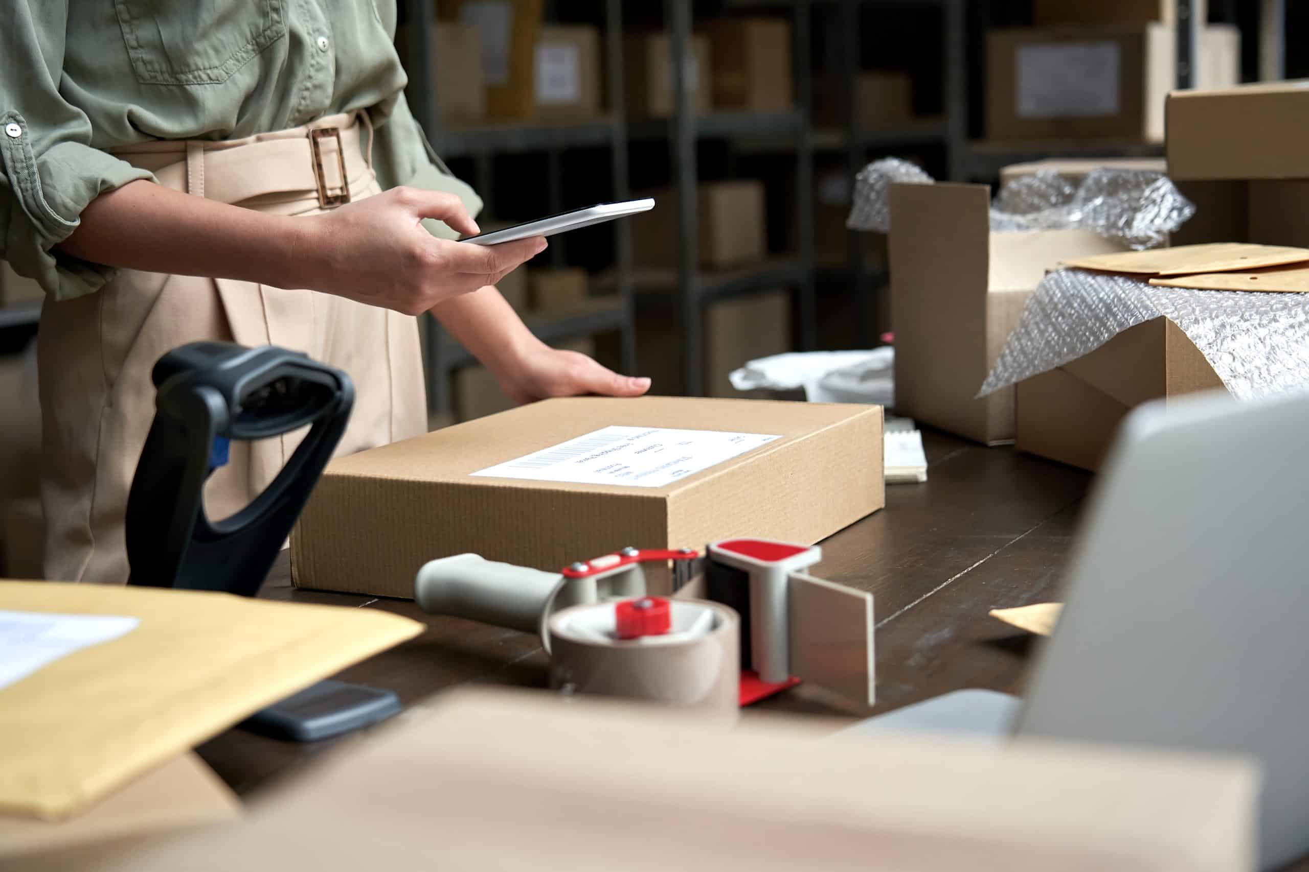 Storage Mitcham - photo shows a small business owner scanning a parcel with their phone, with tape dispenser and boxes on the table