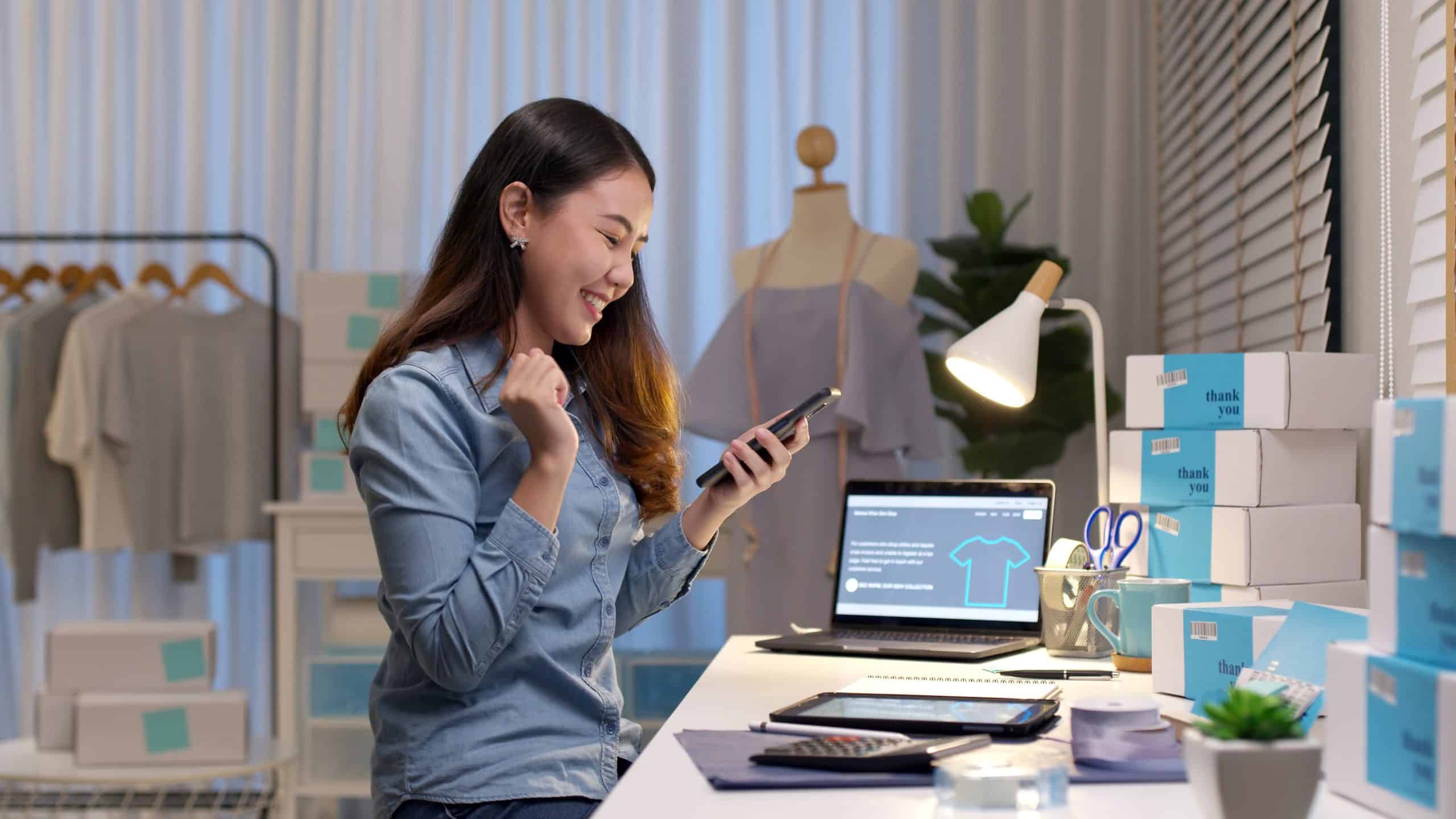 Storage to rent Chippenham - image shows woman business owner sitting at desk and looking at her phone with boxes and clothing rail behind her