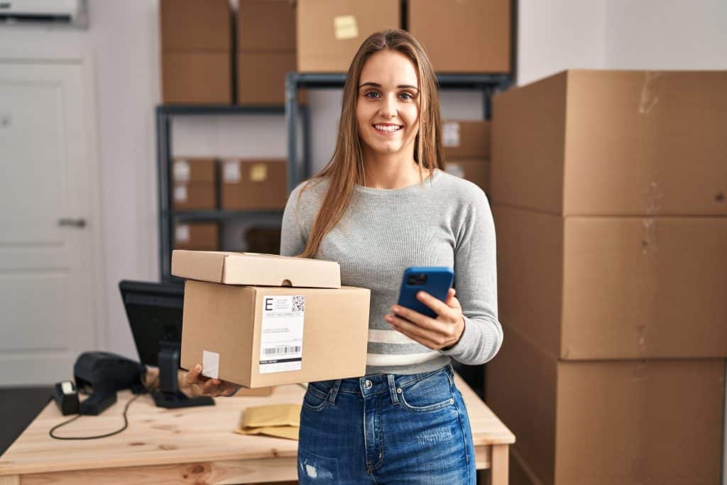 Self storage Chingford - image shows a woman running her e-commerce business holding boxes and a phone, with boxes stacked on shelves behind her