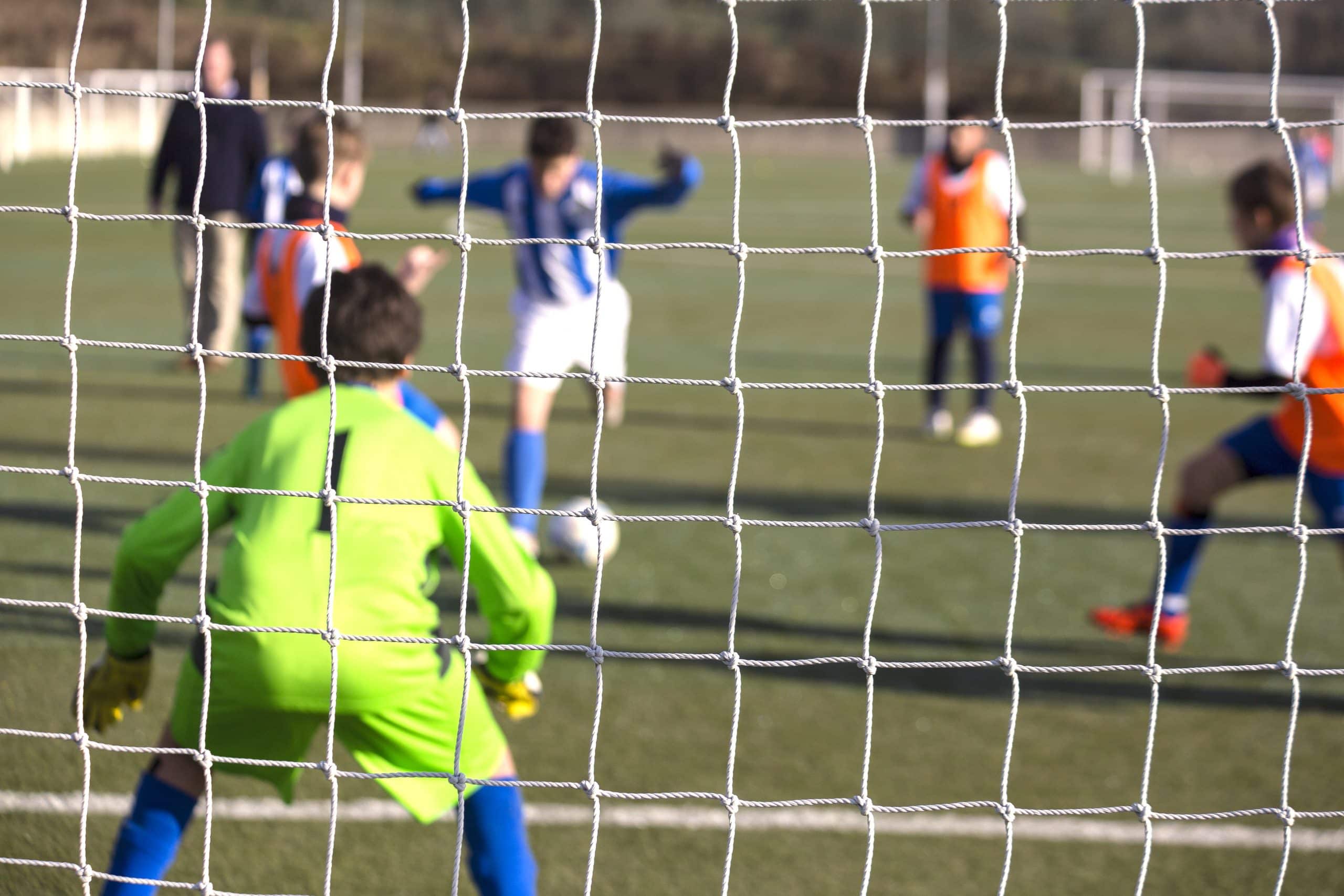 Storage units to rent Brighton - image shows looking through a football goal with a goalie in goal with a green kit and then another player taking a kick on the ball in a blue and white striped kit