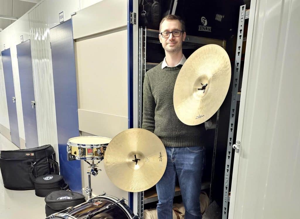 Musician in need of storage space? Our storage Chippenham will help - image shows a customer holding two drum symbols in front of their storage unit