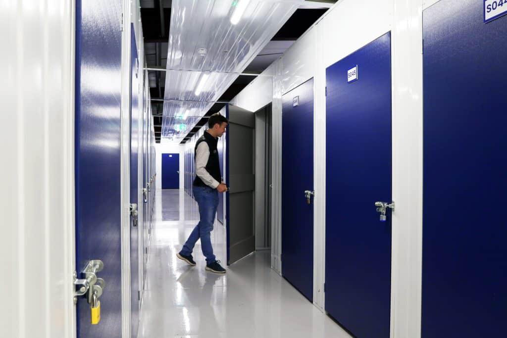 Hectic London Life: Our self storage near Edmonton will bring some peace. Image shows a man opening up a storage unit and a corridor with storage units on both sides. 