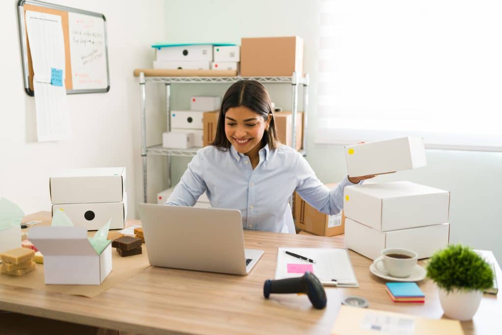 Office Bicester: image shows a woman at her desk looking at her laptop processing online order boxes with shelving and boxes behind her