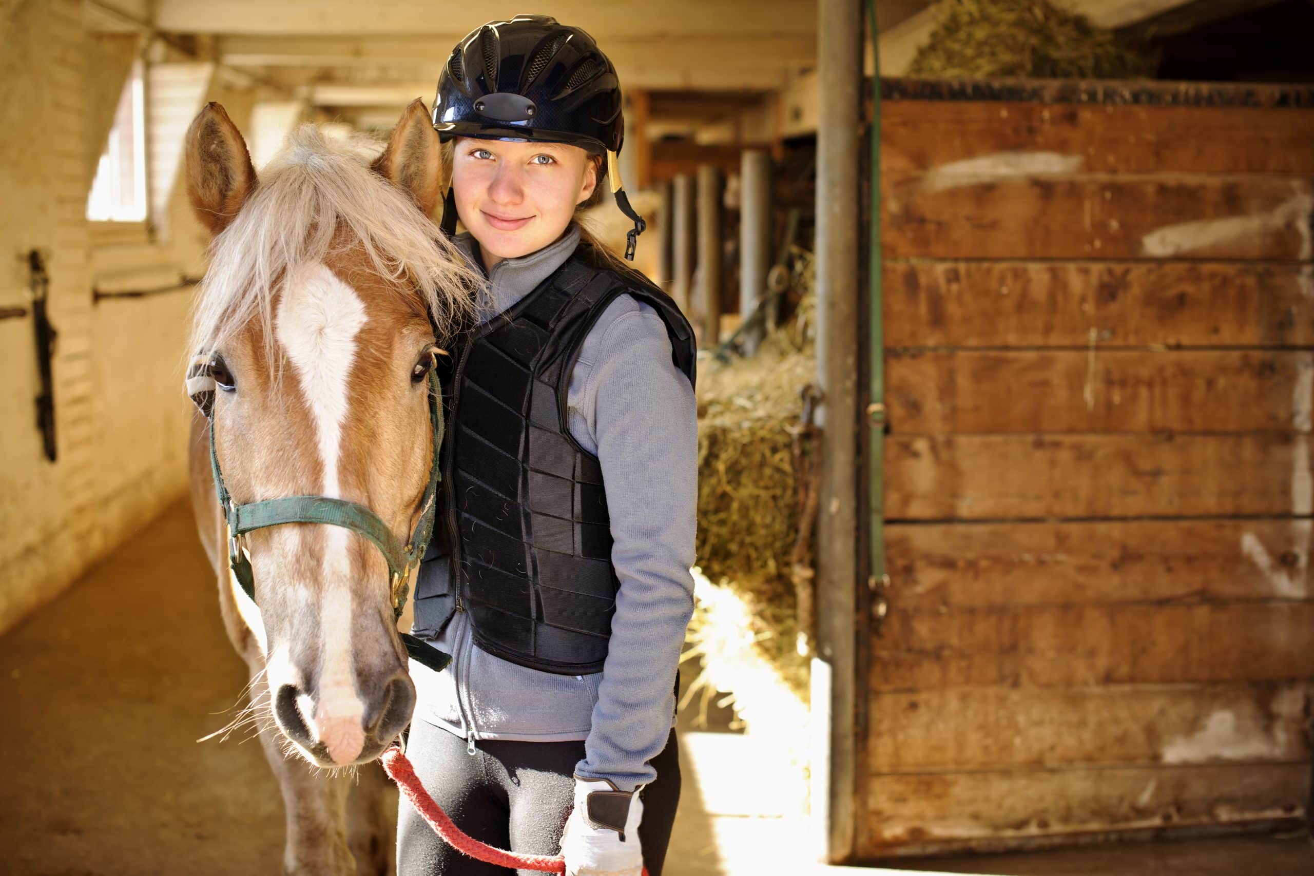 Use our Chingford storage to store your horse essentials. Image shows a girl standing with a horse in the stables wearing a jumping vest, helmet and riding gear.