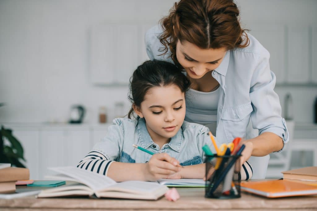 Decided to homeschool? Our storage near Newbury will help you make room. Image shows a mother and a daughter sat at the table with a pen pot and looking at books together. 