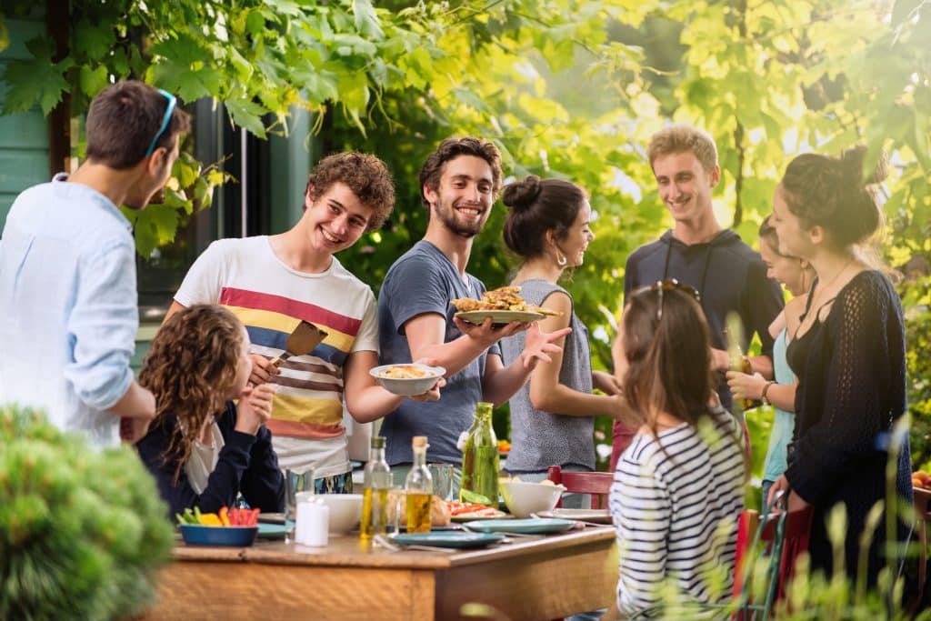 Kids coming home for summer? Our storage unit in Newbury will help. Image shows a group of friends laughing around a table eating food in a garden. 