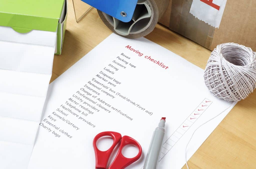 Moving House Storage - image shows a moving checklist printed on a piece of paper laying flat on a cardboard box with scissors, pen and tape gun surrounding it 