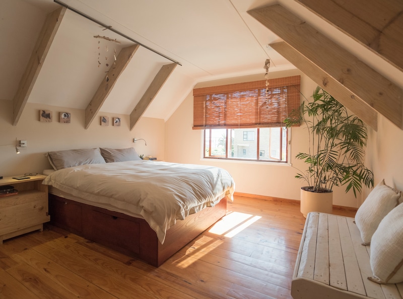 Storage facilities in Mitcham. Image shows the interior of a bedroom with sloping ceilings, wooden floor and cream walls. With a bed in the middle of the room and a potted plant by the window