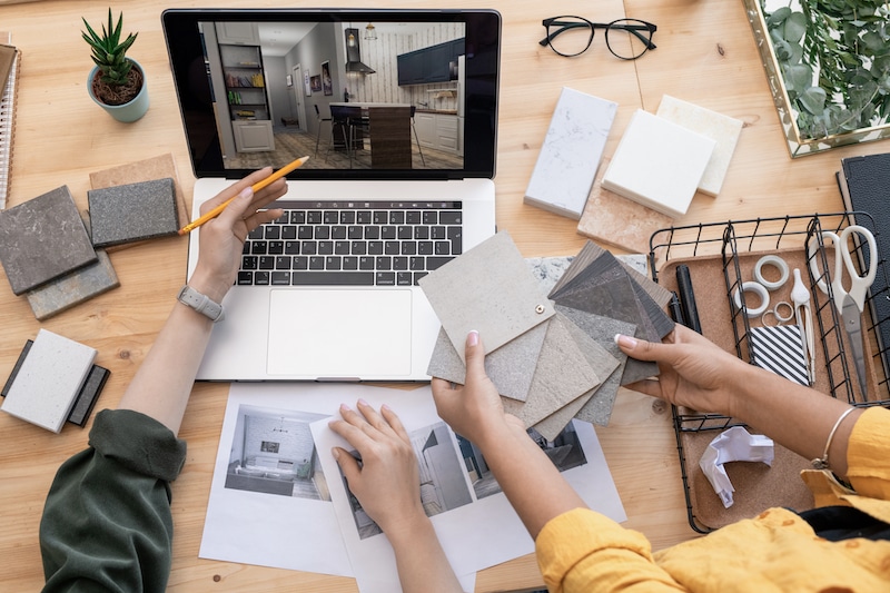 Storage rooms in Mitcham. Image shows an open laptop on a wooden desk with hands holding interior design samples of fabric and someone holding a pencil pointing at the laptop.