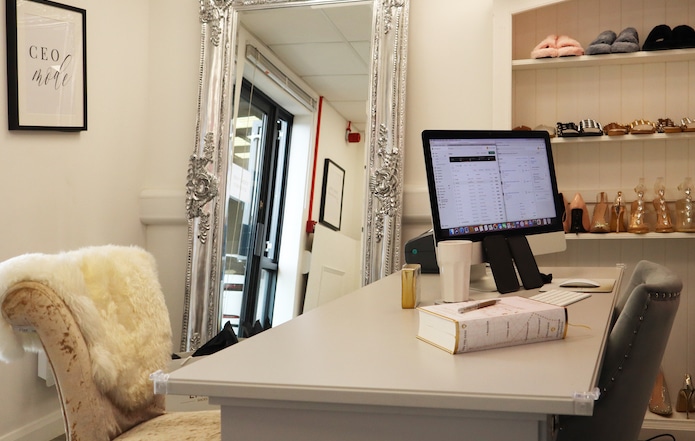 Office to rent Chippenham. Image shows a desk with a screen, book and coffee up. With a silver framed mirror in the background and chair in front of the desk. 