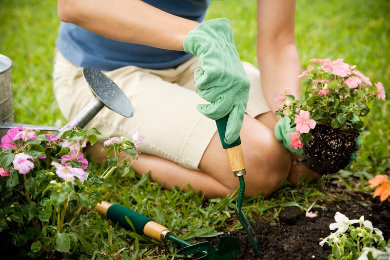 Storage rooms Brentwood. Image shows a person gardening, kneeling on a lawn with pale shorts and a blue top on with a green gardening glove holding a gardening fork. 