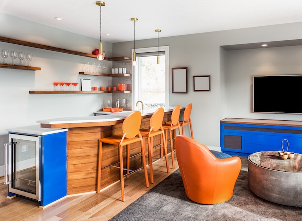 Self storage in Brighton. Image shows an entertainment room with orange chairs at a bar, shelves behind the bar with orange glasses stacked on them and blue cabinets within the room. 