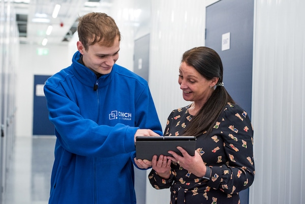 Image shows a cinch storage team member pointing at an ipad with a woman smiling looking at it with him, standing in a corridor of storage units. 