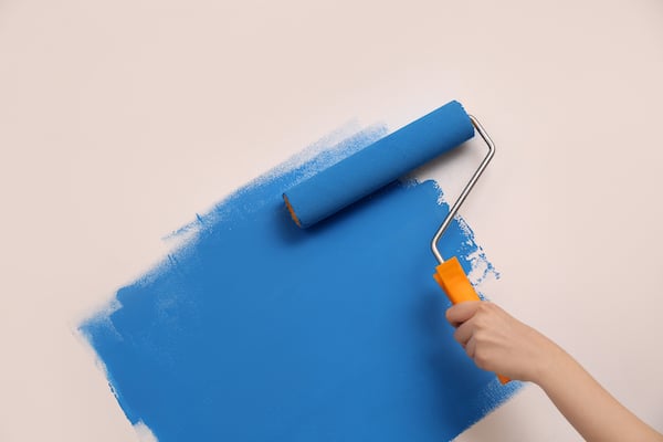 Storage unit Watford. Image shows a paint roller covered in blue paint with an orange handle, painting a wall blue.