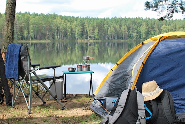 Storage units in Hove. Image shows a campsite set up overlooking a lake with fir trees in the background. With a tent on the right, camping table and camping chair on the left.