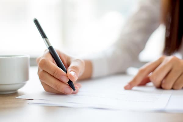 office_chippenham. Image shows an arm holding a black pen onto paper, wearing a top with long white sleeves