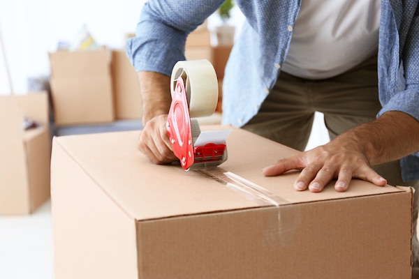 Free cardboard boxes for moving. Image shows a person leaning over a cardboard box applying tape to it. 