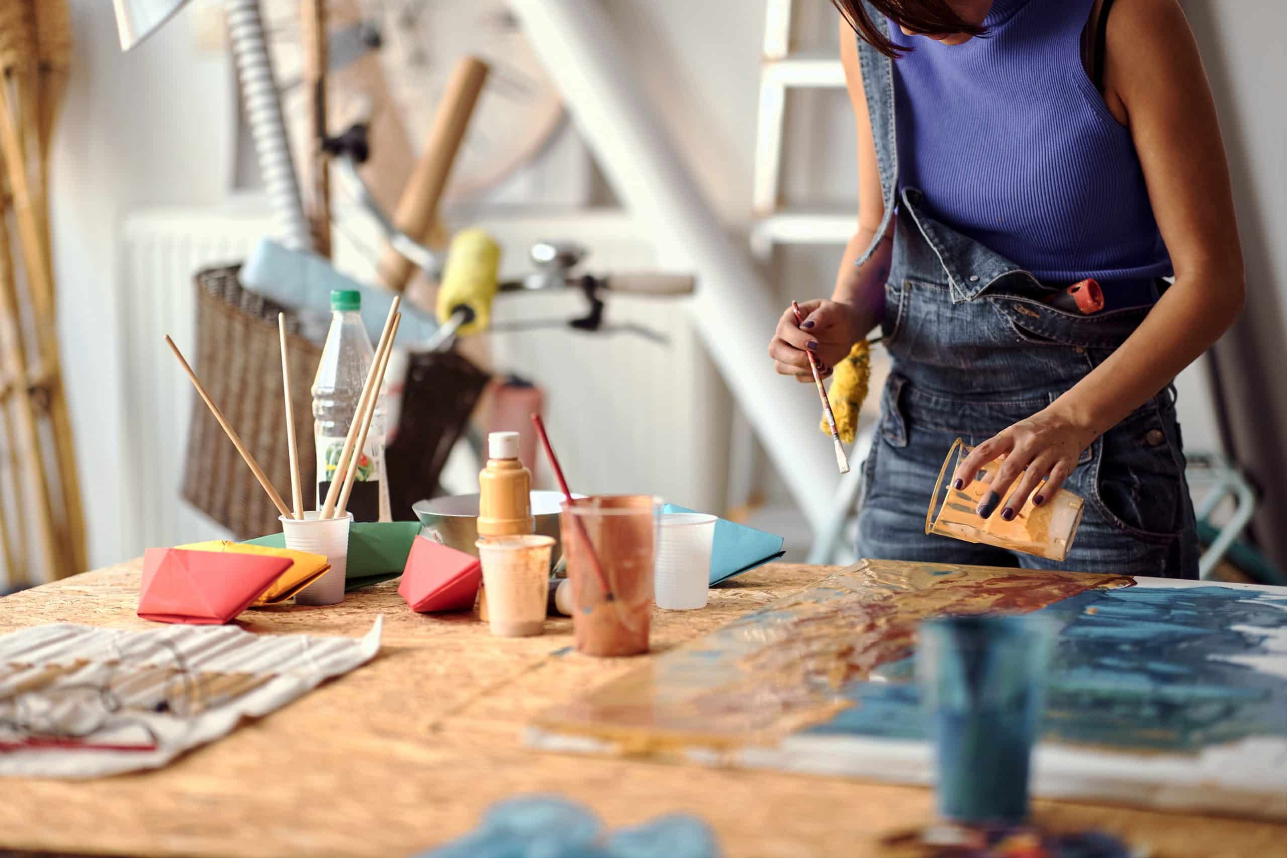 storage_units_in_brighton. Image shows an artist at work in their studio weaing a blue top, with pain pots on a table.