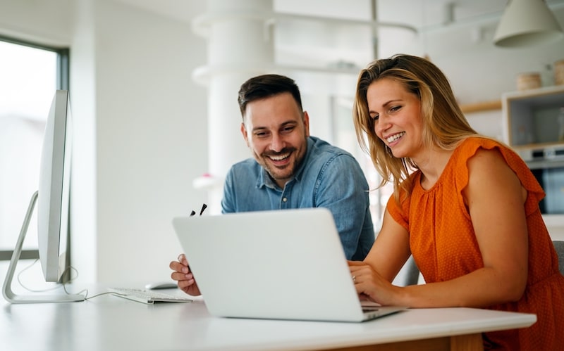 Office to rent in Newbury. Image shows two people at a desk. A woman in an orange top and a man in a blue shirt looking at a silver laptop.