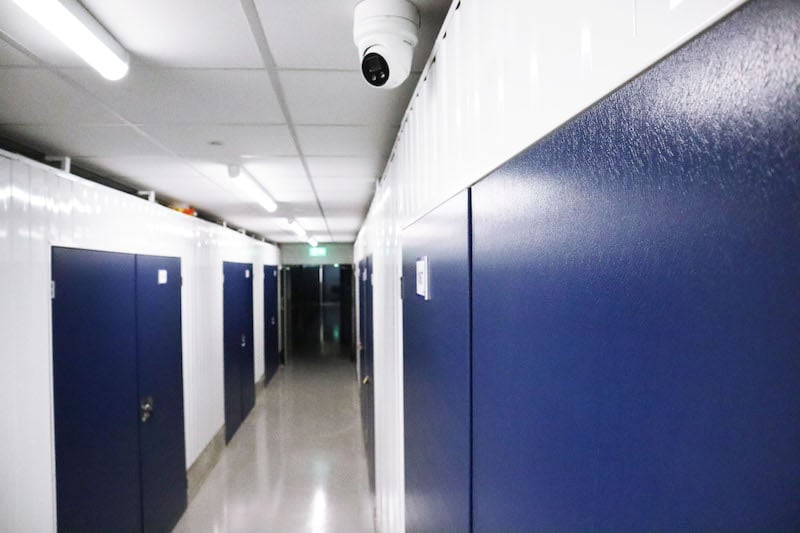 Storage in Seaford. Image shows the corridor of the storage unit facility with storage units with blue doors and a white CCTV camera.