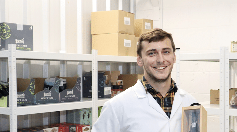 Image shows a male business owner in their storage unit with food goods stacked on shelving behind them.