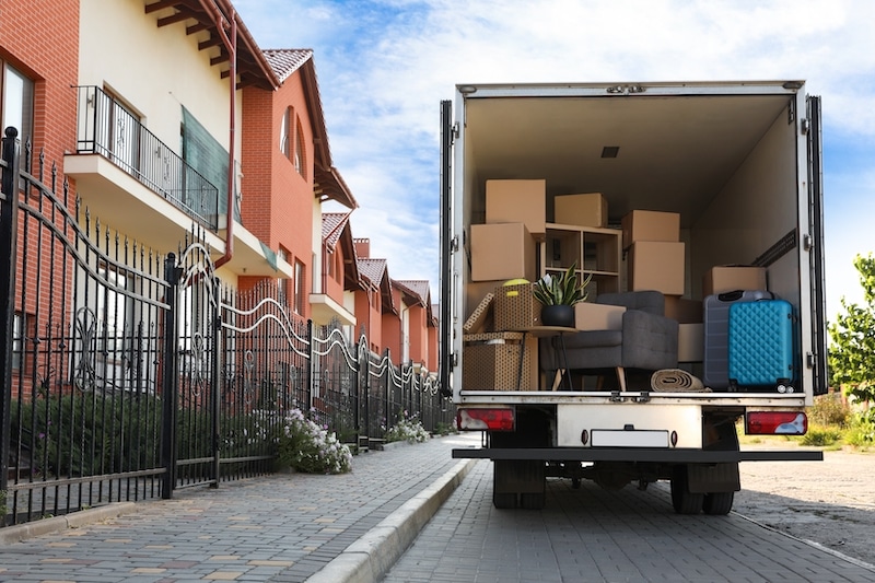 Self storage in Woking. Image shows a removal van with open doors at the back filled with household belongings and a row of houses with red brick and cream brick to the left