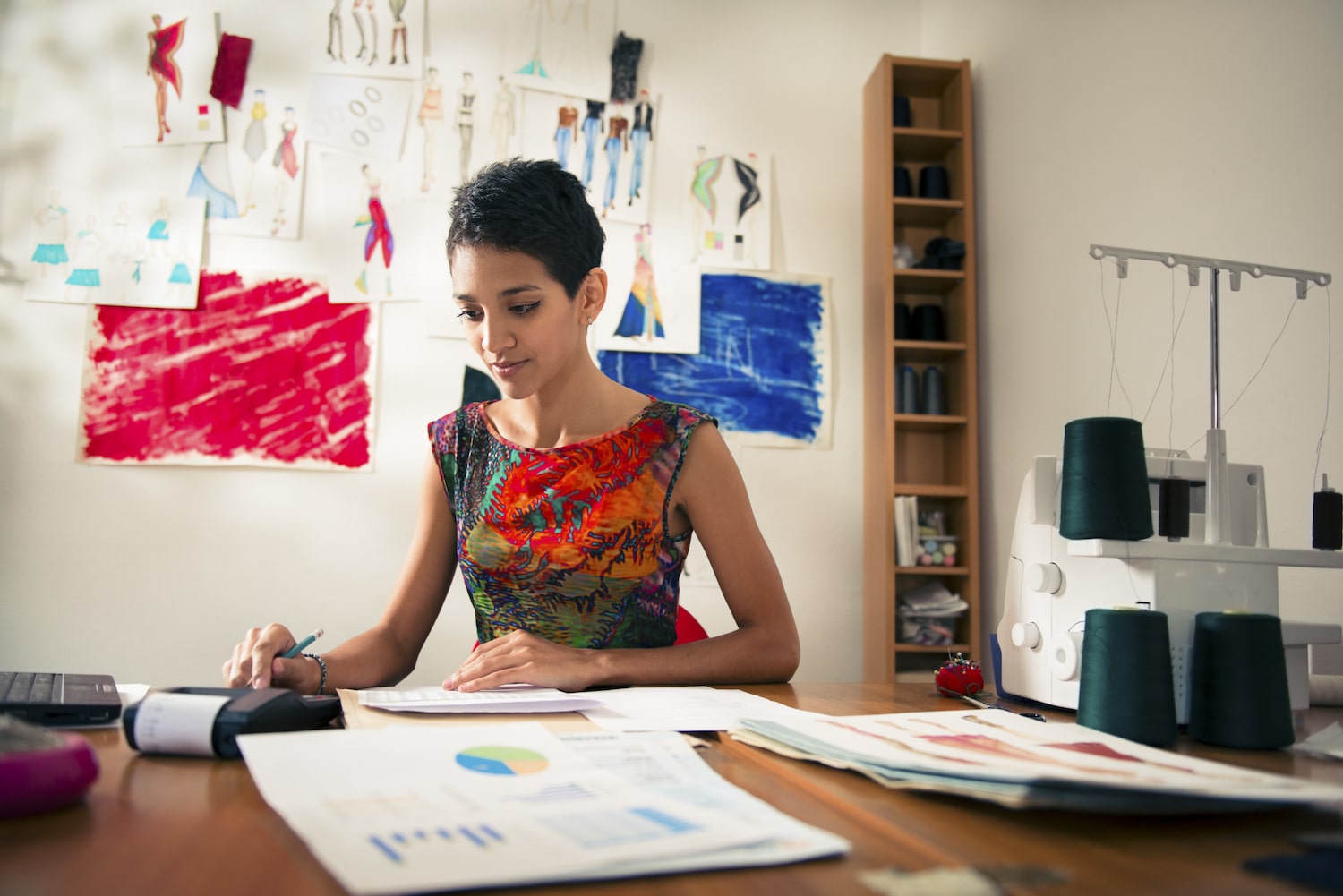 How to find the right office to rent Mitcham. Image shows a woman sitting at her desk in a colourful top with sketches on the wall behind her and a sewing machine on the desk.