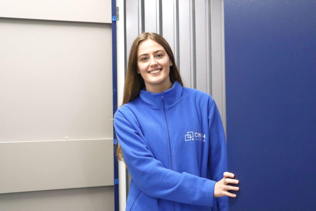 How to pack a self storage unit. Image shows a Cinch Self Storage employee standing in the doorway of a storage unit wearing a blue Cinch Self Storage fleece. 