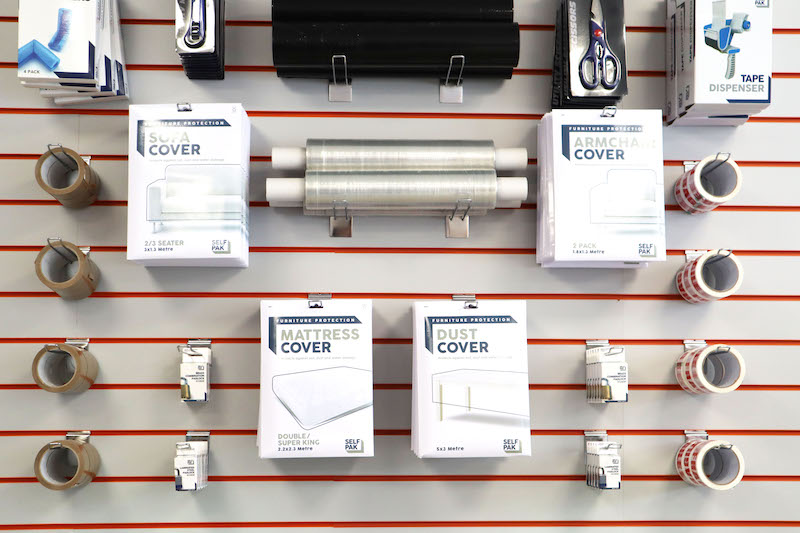 5 Essential house moving supplies. Image shows dust covers, tape and other moving essentials displayed on a wall.