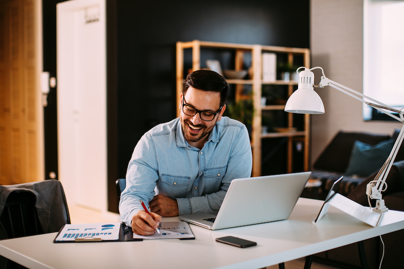 Office to rent in Sidcup. Image shows a young business man in a blue shirt, sitting at a desk working at home with laptop and papers on desk