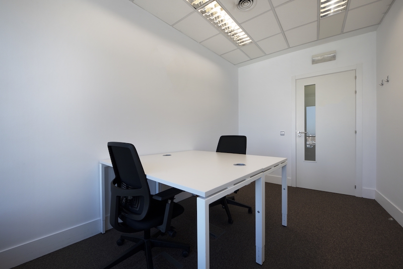 Small office to rent Newmarket. Image shows an office with double white wooden desks, black swivel chairs and a door with elongated glass
