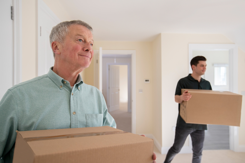 Storage units in Swindon. Image shows a senior man holding removal boxes with a removal helper in the background.